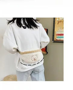 Detail of white plush waist bag featuring animal embroidery and khaki shoulder strap