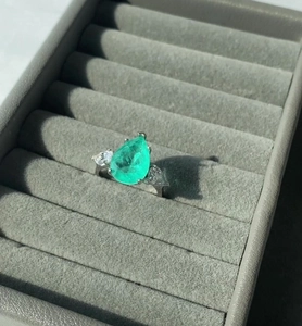 Macro detail of pear-cut green gemstone ring with side stones in a jewelry box
