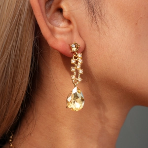 Close-up of elegant gold drop earrings with pear-shaped yellow crystals and diamond accents