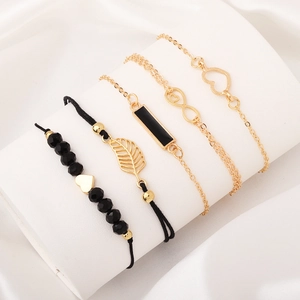 5-piece gold and black bracelet set with heart, leaf, and infinity charms on white silk