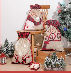 Three Christmas drawstring gift bags with Santa and reindeer motifs on wooden decor