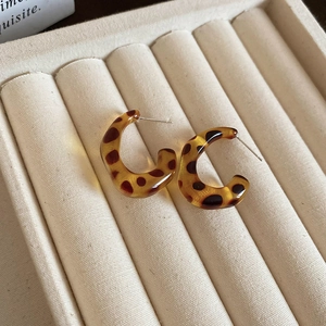 Macro view of C-shaped amber leopard print resin earrings on a beige velvet tray