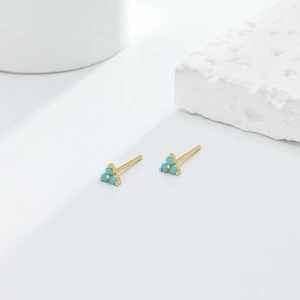 Detailed close-up of gold triangle stud earrings with turquoise stones on white decor