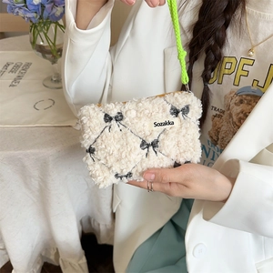 Detail of cream fleece makeup bag with black bow embroidery and green braided strap