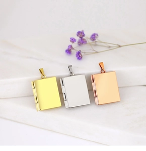 Polished book-shaped locket pendants in gold, silver and rose gold on marble