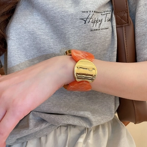 Gros plan d'un bracelet en métal doré et résine marbrée orange porté au poignet
