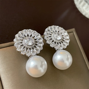 Close-up of flower zircon earrings with white faux pearls on a champagne gift box