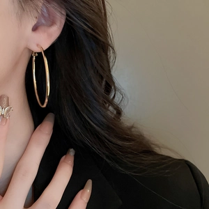 Close-up of a model wearing large minimalist golden hoop earrings with a sleek finish