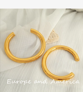 Detail of gold C-shaped chunky bangles resting on white silk and decorative stones