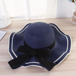 Detail of a dark blue straw sun hat with a large black bow and white striped brim edge