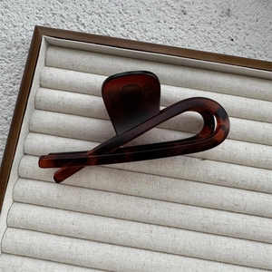Close-up of a large tortoiseshell hair claw clip with twisted design on velvet display tray