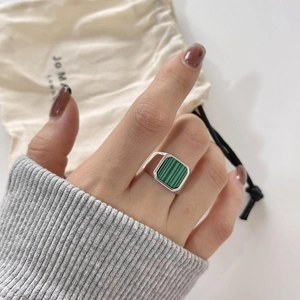 Detailed view of wide silver ring with square malachite stone worn on finger