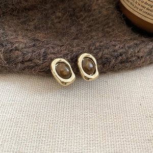 Detailed view of vintage gold-rimmed oval tiger eye stone earrings on linen texture