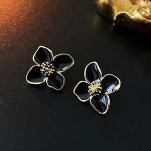 Makroaufnahme eleganter schwarzer Emaille-Blumenohrringe mit Goldbeschichtung auf Textur