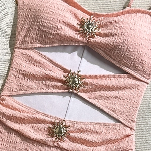 Detail of pink crinkle swimsuit fabric with hollow cut-outs and golden sun metal charms