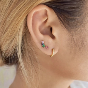 Close-up of a silver wing cartilage stud with colorful zircons and a gold hoop earring