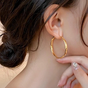 Close-up of model wearing 18K gold-plated large circular hoop earrings with metallic finish