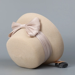 Dettaglio di cappello cloche in paglia beige con grande fiocco e cordino antivento