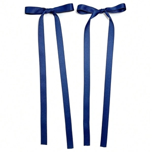 Detail of two navy blue satin ribbon bow hair clips with long streamers on white backdrop