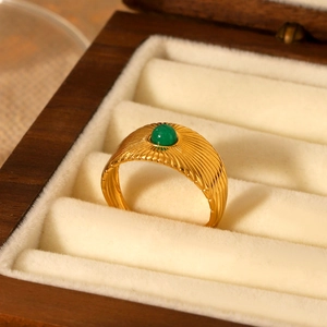 Detail of vintage gold-plated ring with green natural stone on beige velvet cushion