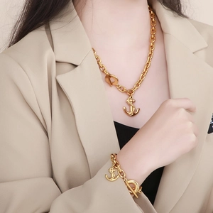 Close-up of a gold anchor pendant necklace and bracelet set worn by a fashion model