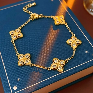 Detail of a gold clover bracelet with five zircon flower charms on a navy jewelry box