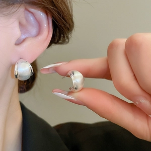 Detailed close-up of matte silver hoop earrings showing textured finish and small curved design