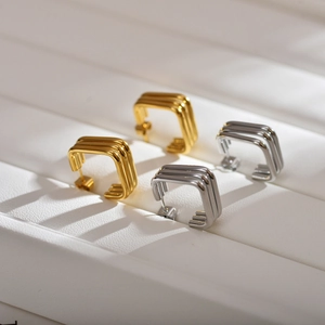 Macro shot of gold and silver layered square geometric hoop earrings on leather background