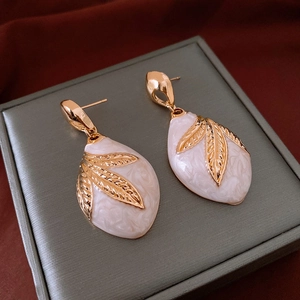 Detailed macro view of retro leaf earrings with white marble texture and gold metal accents