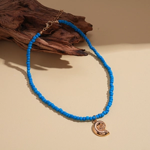 Detailed close-up of blue beaded necklace featuring a golden conch shell pendant on driftwood