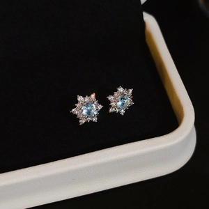 Macro shot of silver flower stud earrings with a blue gemstone and zircon halo