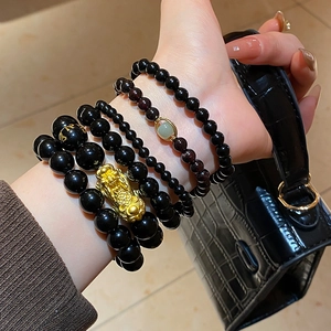 Detail of stacked obsidian bead bracelets with gold Pi Xiu and garnet accents on wrist