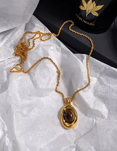 Macro detail of the oval tiger eye pendant on a thick gold twisted rope chain necklace