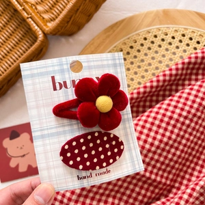 Detail of a red plush flower hair clip and white polka dot clip on a display card
