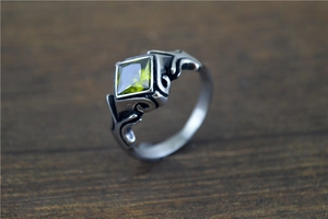 Detail of vintage rhombic olive green gemstone set in gothic scroll textured steel ring