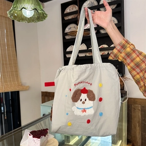 Detail of grey canvas tote bag featuring Puppy Land embroidery and drawstring closure