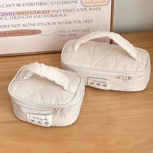 Detail of cream quilted makeup bag set with top handles on a cozy wooden desk