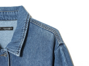 Detail view of blue denim jacket collar and shoulder stitching with golden thread