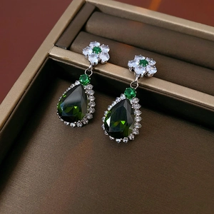 Detail of silver earrings with drop-shaped green zircon stones and white crystal petals