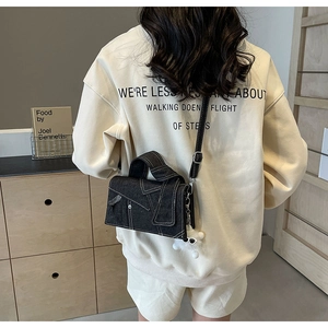 Détail du sac bandoulière en denim noir avec surpiqûres blanches et charm en peluche