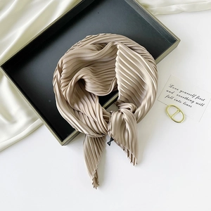 Detail of champagne gold pleated silk scarf tied in a bow on an elegant flat lay display