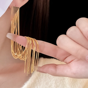 Close-up of golden triangle earrings with long snake chain tassels on a model