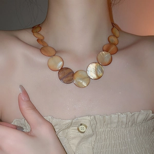 Close-up of pearl shell necklace with amber gradient discs worn on a pleated top