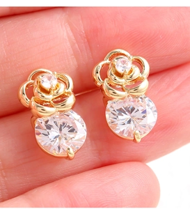 Détail de boucles d'oreilles rose dorée avec zircone tenues entre les doigts