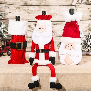 Three Santa Claus velvet wine bottle covers displayed on a rustic wooden background