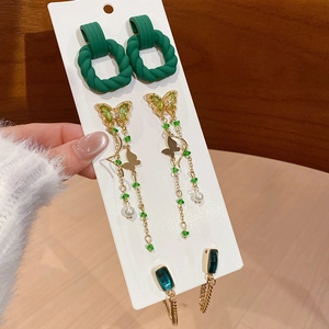 Detailed view of green acrylic earrings set with gold butterfly and pearl charms