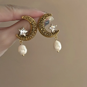 Gros plan de boucles d'oreilles lune et étoile dorées avec perle baroque