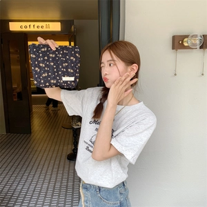 Detail of floral quilted cotton pouch with gold label held by a model in a cafe