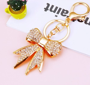 Close-up of golden bow-shaped keychain with sparkling rhinestones on a pink surface