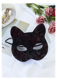 Detail of a cat face mask with red and silver glitter floral patterns on black velvet